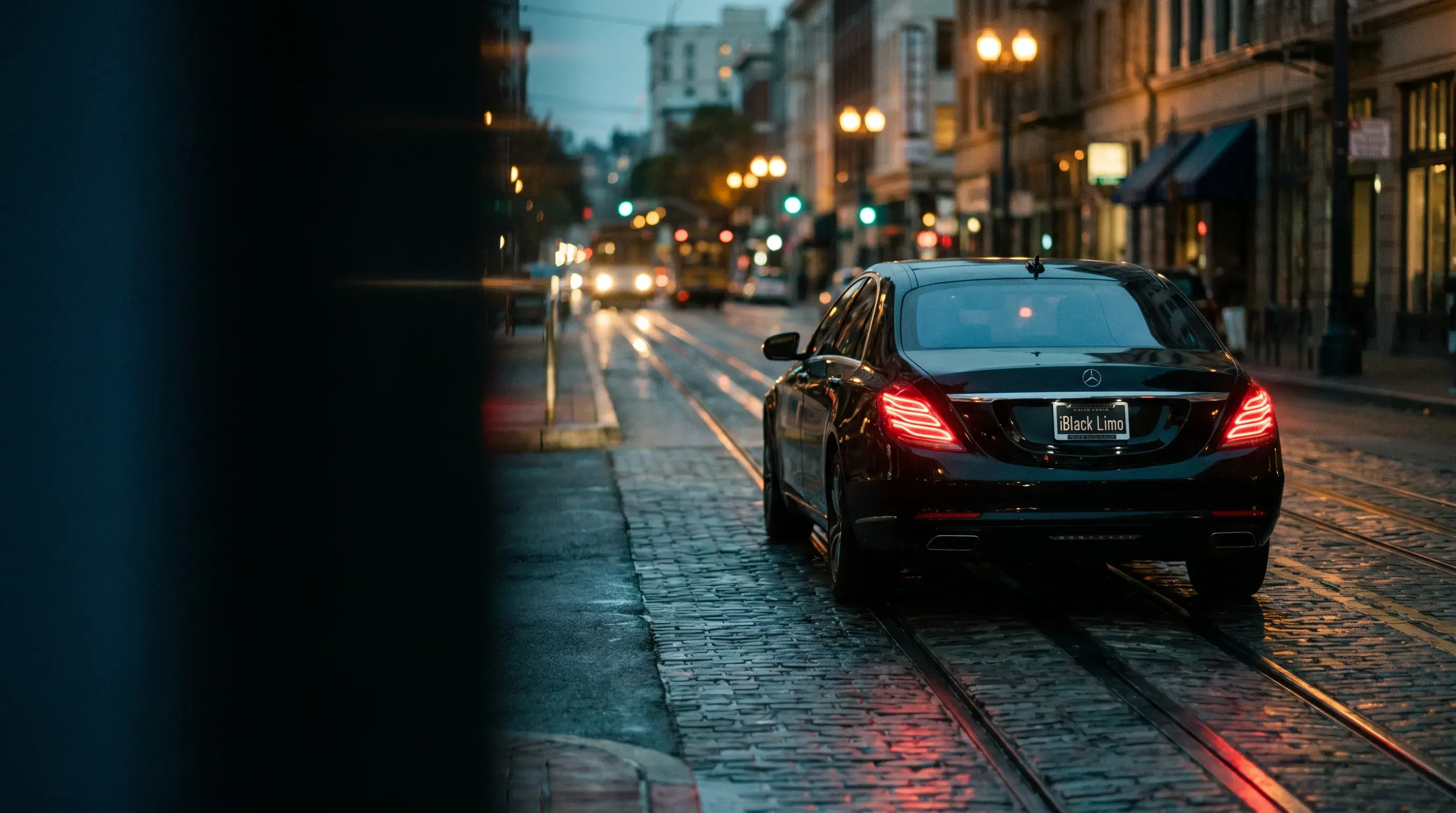 A black sedan receding down a wet city street at night